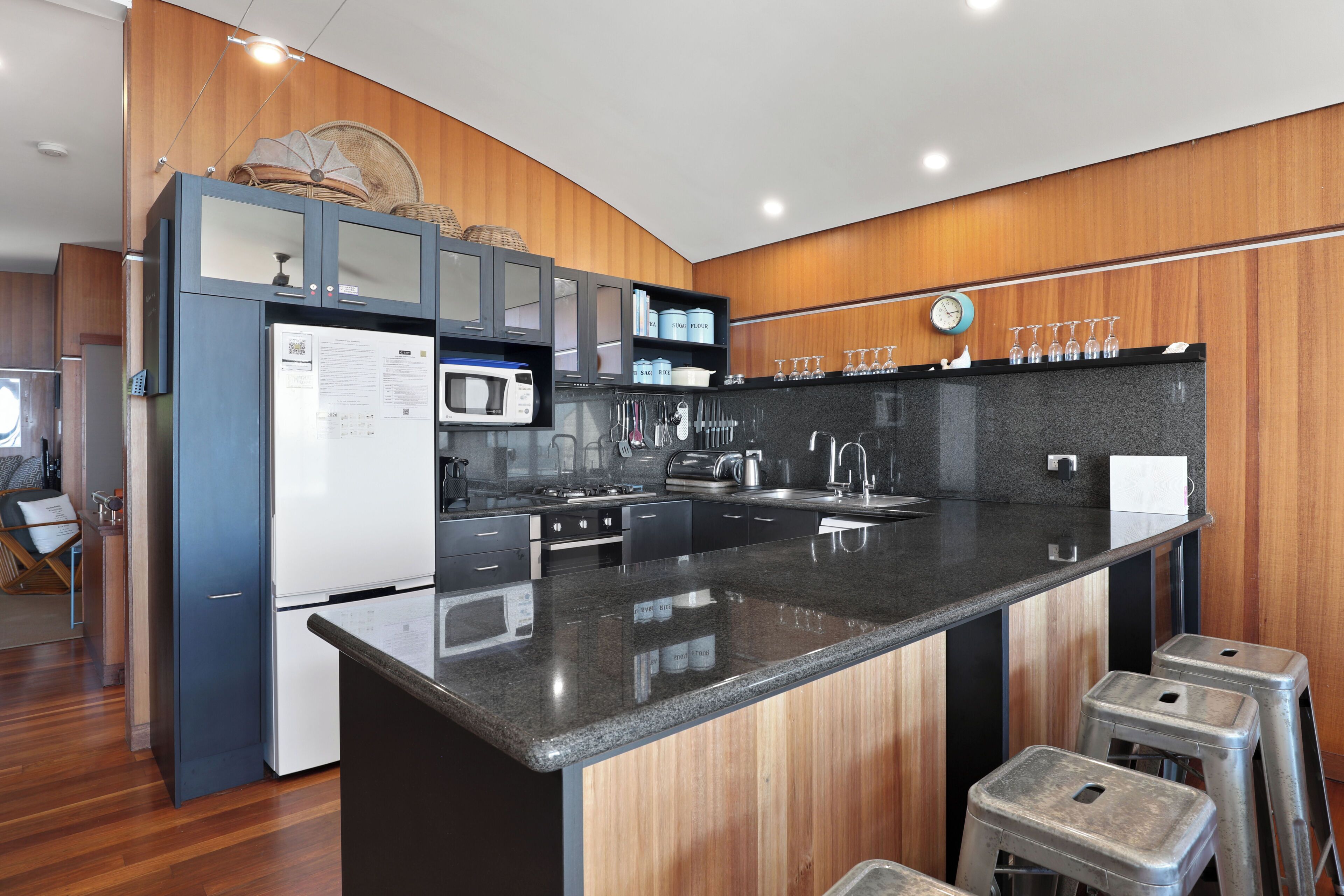 A modern kitchen with a central island, stainless steel appliances, wooden paneling, and a bar stool area.