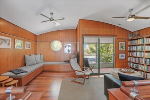 A modern living room with wooden paneling, a built-in bench, a rocking chair, a bookshelf, and two ceiling fans. - Panoramic views from this beautifully furnished unit set high on the hill. (Point Lookout)