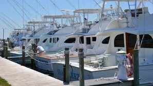 A marina with several yachts docked, wooden walkways, and a person working on a boat.