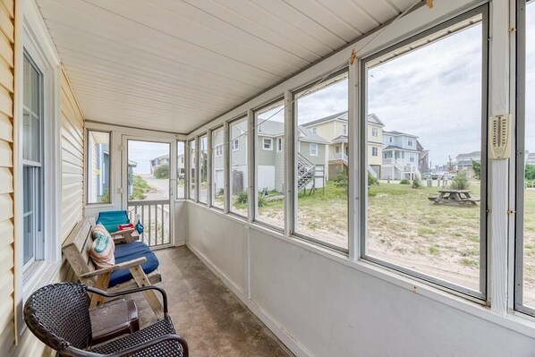 A covered porch with a view of houses and a picnic table in the background.