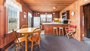 A wooden cabin with a dining area, kitchen, and a sign reading "BEACH HOUSE".
