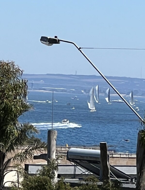 Blick auf die Küste mit Segelbooten auf dem Wasser, einer Straßenlaterne und einer Brücke im Hintergrund.