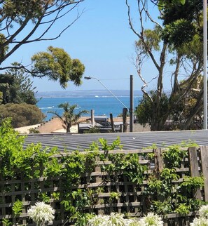 A coastal view with a wooden fence and greenery in the foreground, leading to a beach and ocean in the background. - Portsea - Bay views secluded homely property:2 minutes walk Portsea Hotel Beach (Portsea)
