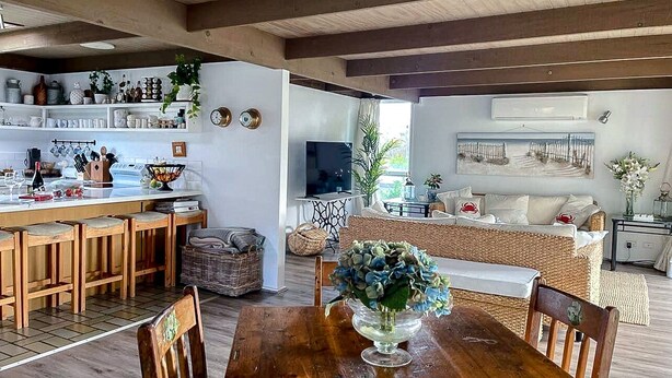 Eine geräumige Küche mit Holzhockern, einem Esstisch mit Stühlen und einem Fernseher im Hintergrund.