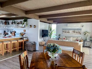 Eine geräumige Küche mit Holzhockern, einem Esstisch mit Stühlen und einem Fernseher im Hintergrund.