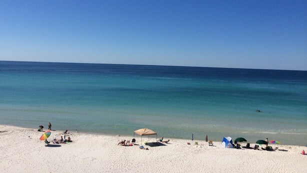 A beach with clear blue water, white sand, and several beach umbrellas. - Three Bedroom Beachfront Condo at Pinnacle Port  (Panama City Beach)