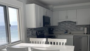 A modern kitchen with white cabinets, a black refrigerator, and a view of the ocean through a large window. - Three Bedroom Beachfront Condo at Pinnacle Port  (Panama City Beach)