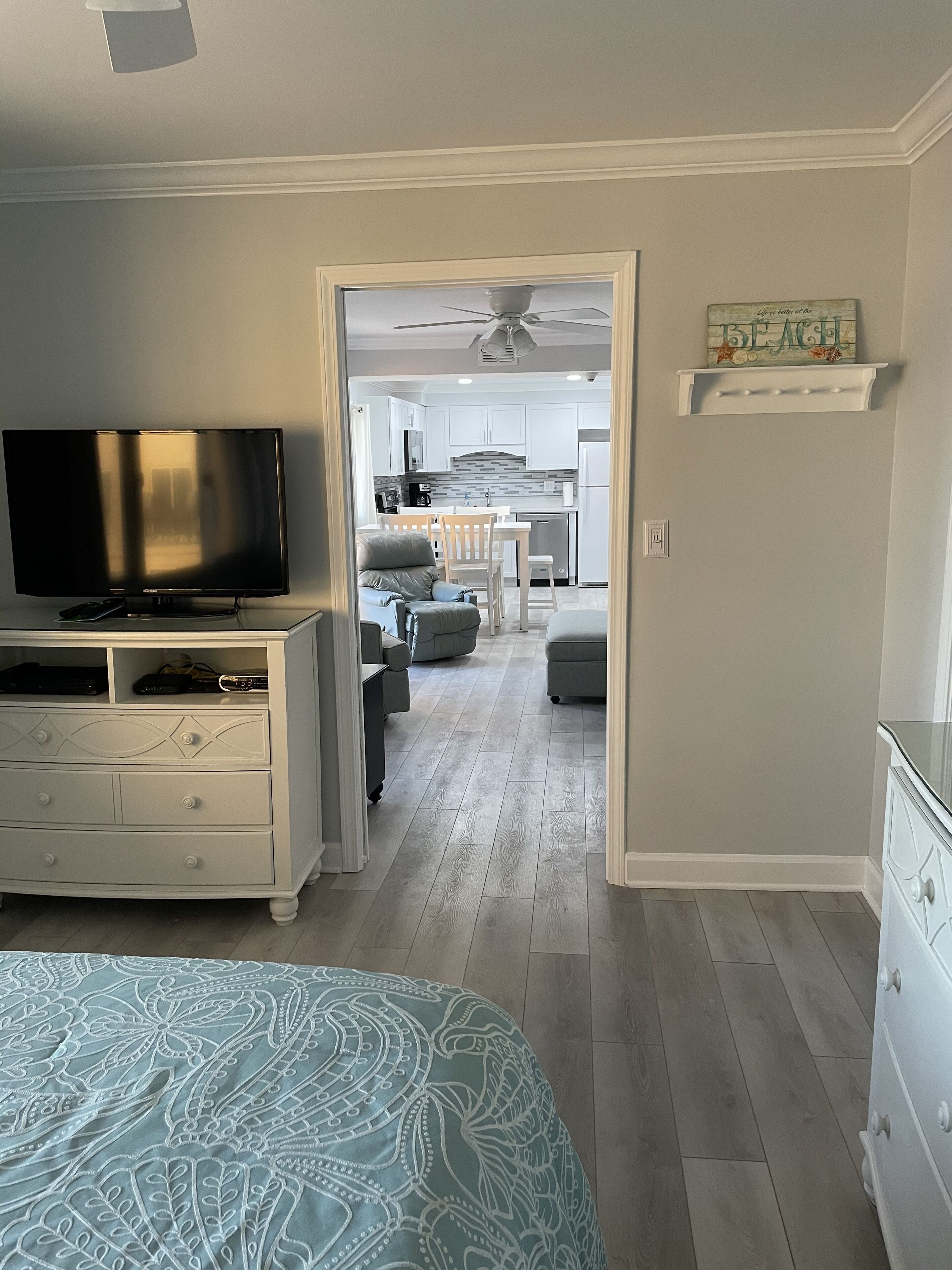 Un dormitorio con cama, televisor y cómoda. Hay un pasillo que conduce a una cocina y una sala de estar.