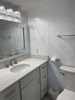 A bathroom with a white vanity, a large mirror, a toilet, and a trash can. - Three Bedroom Beachfront Condo at Pinnacle Port  (Panama City Beach)