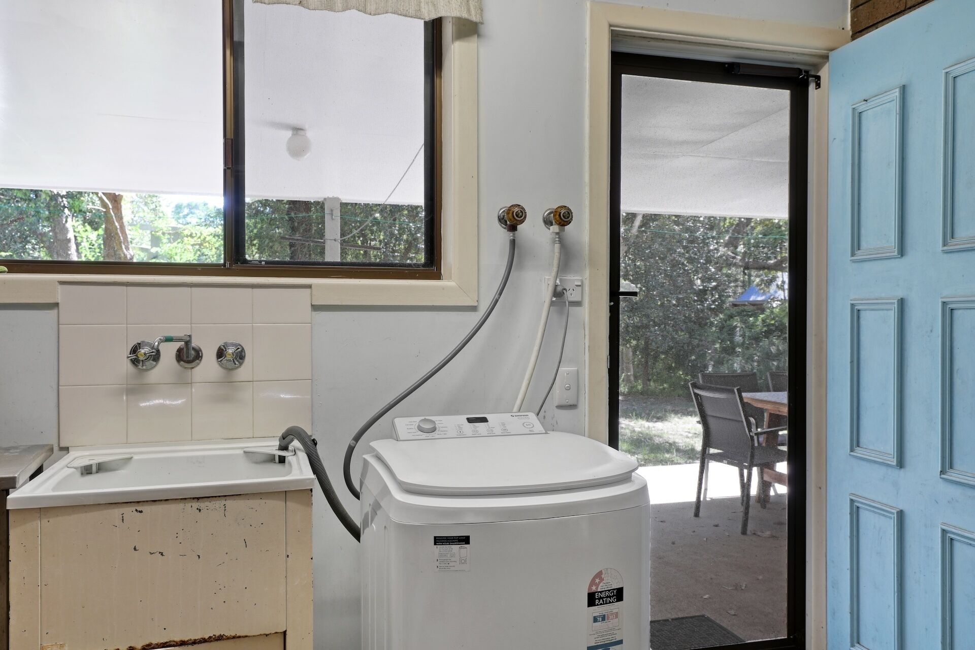 A compact kitchen with a sink, a white washing machine, and a window with a view of greenery.