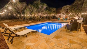 A swimming pool with lounge chairs and string lights, surrounded by stone patio and trees. - ATX Hideaway - Heated Pool / Jacuzzi / Firepit / Sleep 14 (Austin)