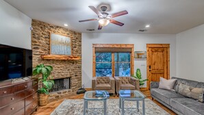 A living room with a stone fireplace, a ceiling fan, a TV, and a couch. - ATX Hideaway - Heated Pool / Jacuzzi / Firepit / Sleep 14 (Austin)