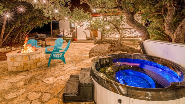 An outdoor patio with a stone floor, a hot tub, and two blue chairs. - ATX Hideaway - Heated Pool / Jacuzzi / Firepit / Sleep 14 (Austin)