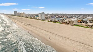 Una amplia playa arenosa con olas del océano, edificios frente al mar y un cielo despejado.