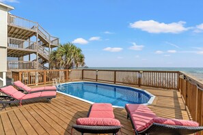 A wooden deck with a pool, lounge chairs, and a view of the ocean.