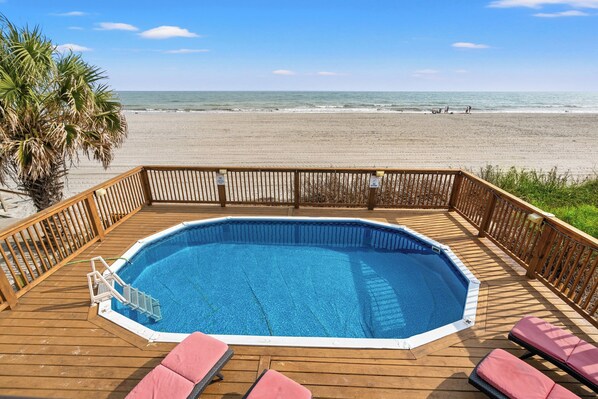 Une terrasse en bois avec une piscine, des chaises longues et un palmier.