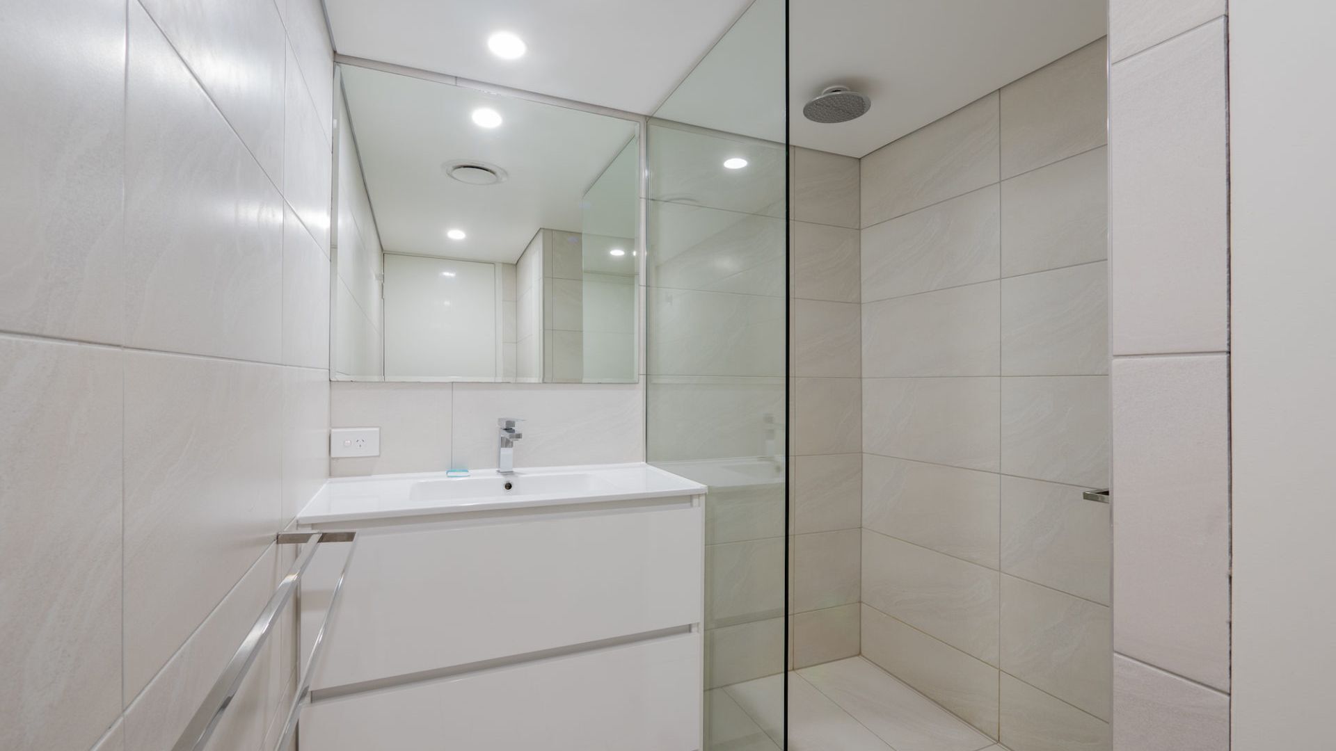 Un baño moderno con cabina de ducha de vidrio, un lavamanos blanco y un espejo grande.