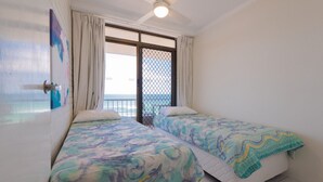 Una habitación con dos camas, una ventana con cortinas, vista al mar y un ventilador de techo.