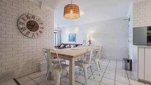 Una cocina moderna con paredes de ladrillo blanco, una mesa de comedor de madera con sillas blancas, un lámpara colgante y un gran reloj de pared.