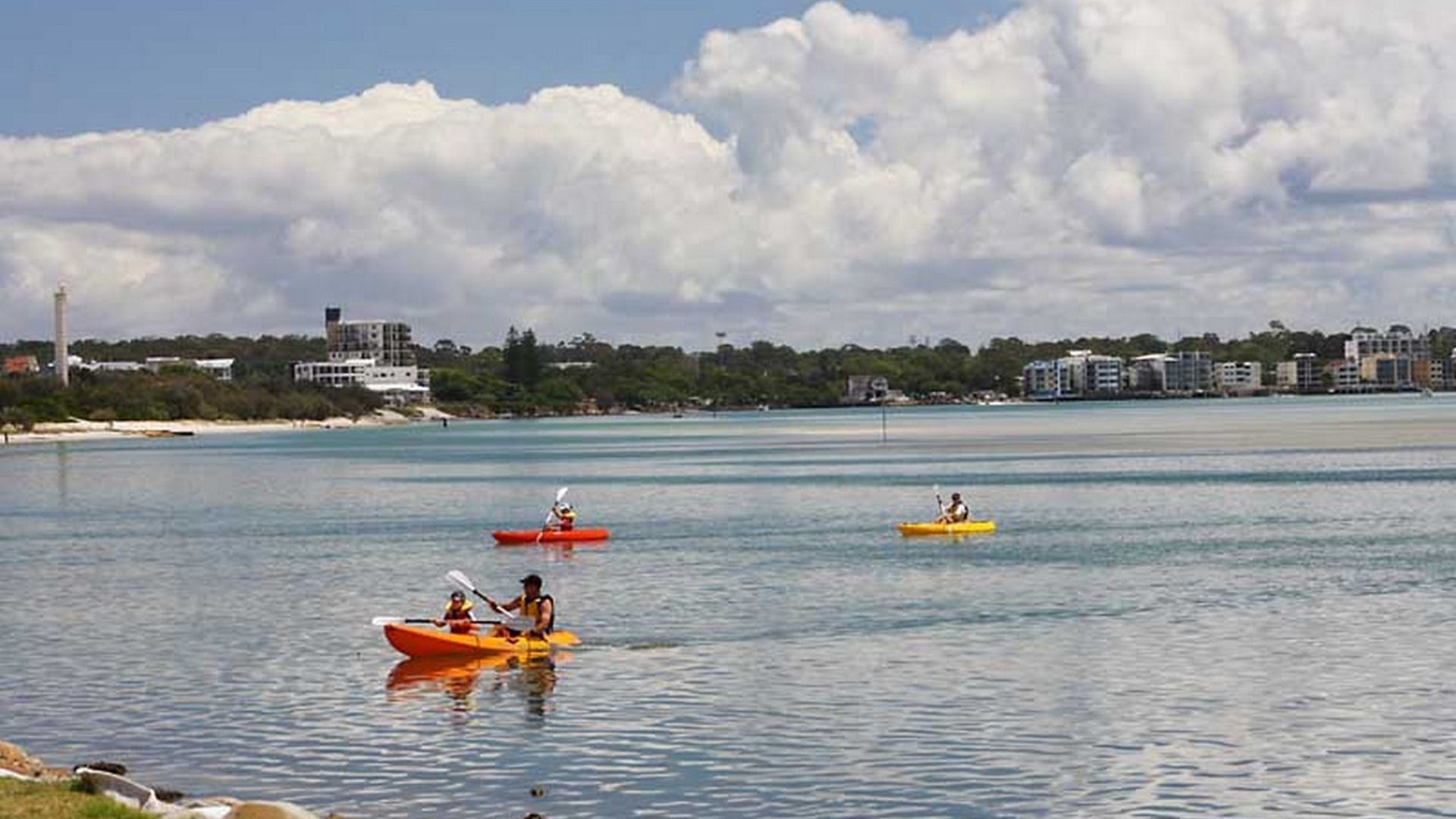Una orilla tranquila con kayaks y un horizonte urbano distante.