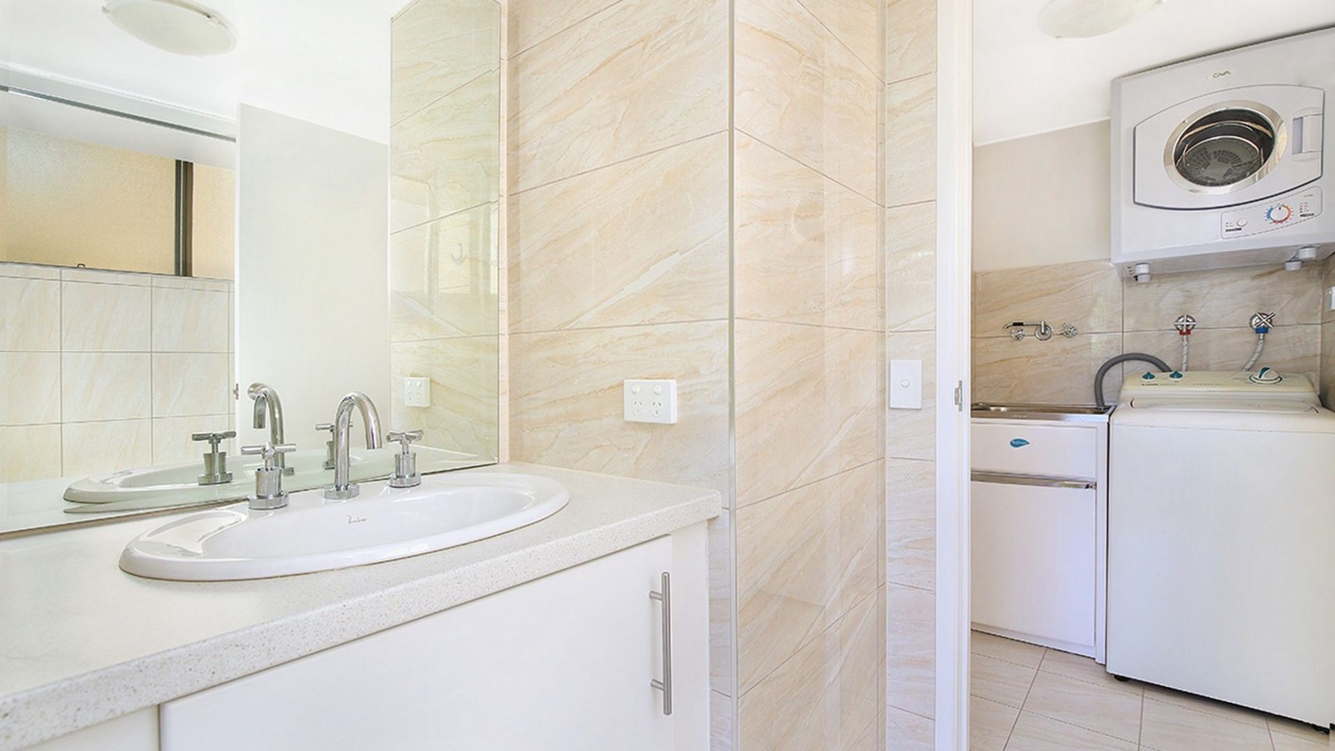A modern bathroom with a double sink, a mirror, a washing machine, and a toilet.