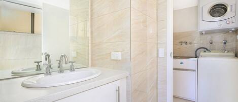 A modern bathroom with a double sink, a mirror, a washing machine, and a toilet.