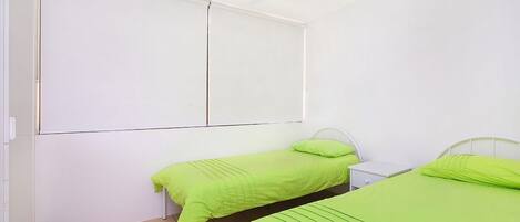A room with two beds, each with green bedding, a white headboard, and a small bedside table.