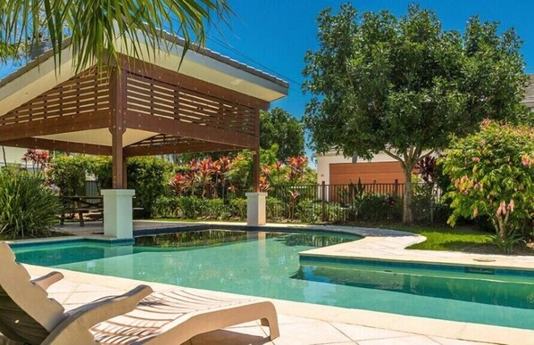 A swimming pool with lounge chairs, a pergola, and lush greenery. - Seadrift 31 on Browning Street (Byron Shire)