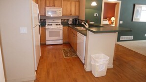 A compact kitchen with wooden cabinets, a microwave, stove, and dishwasher. - I'll Be Back Ski in/out condo (bellaire)