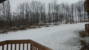 A snow-covered outdoor area with a wooden deck and a view of leafless trees. - I'll Be Back Ski in/out condo (bellaire)