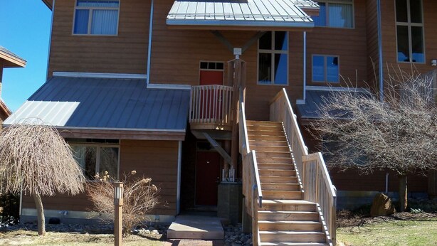 A two-story building with a wooden exterior, a metal roof, and a staircase leading to the upper floor. - I'll Be Back Ski in/out condo (bellaire)