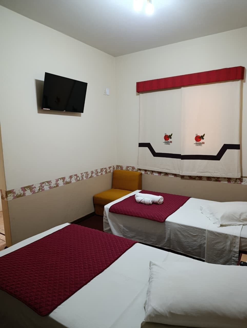 A hotel room with two beds, a television on the wall, and a red and white curtain.