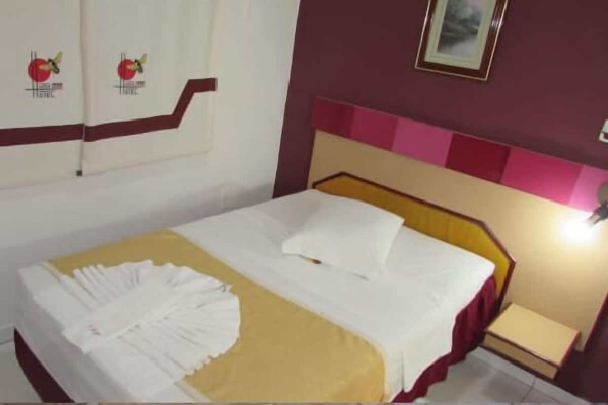 A hotel room with a bed, a nightstand, and a wall-mounted picture.