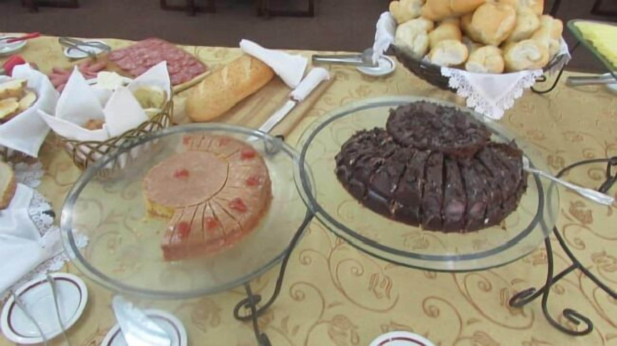 A buffet table with various food items including a chocolate cake, a fruit tart, and several types of bread.