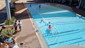 An outdoor swimming pool with clear blue water, surrounded by shaded areas and a wooden deck. - West Beach Lagoon 202 - Quiet & Ground Floor! (Scarborough)