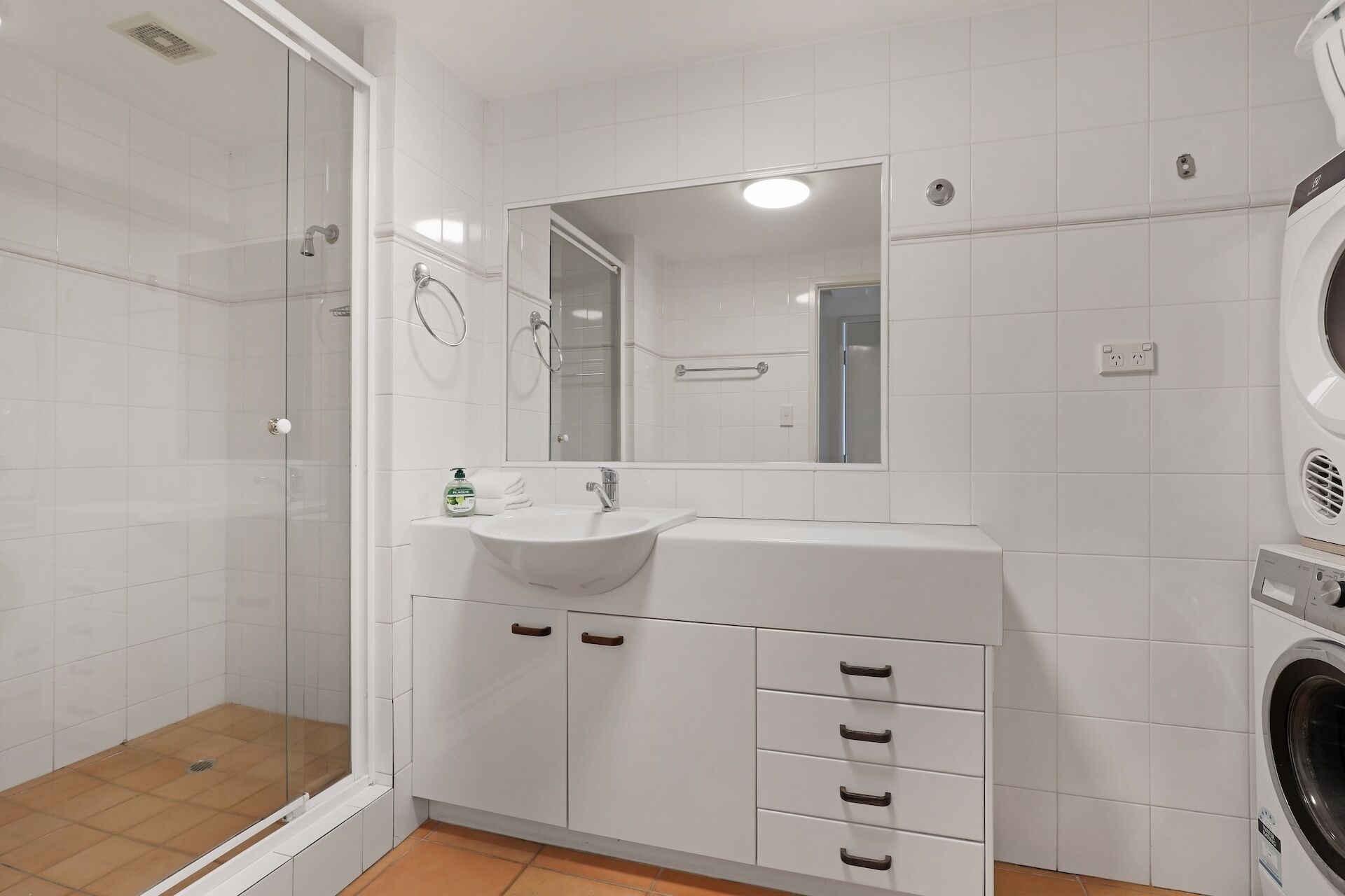 A modern bathroom with a glass shower enclosure, a sink with a mirror, and a built-in washing machine.