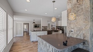 A modern kitchen with a central island, pendant lighting, and a stone accent wall. - A Sunset Dream - Monthly Beach Rental (Clearwater Beach)
