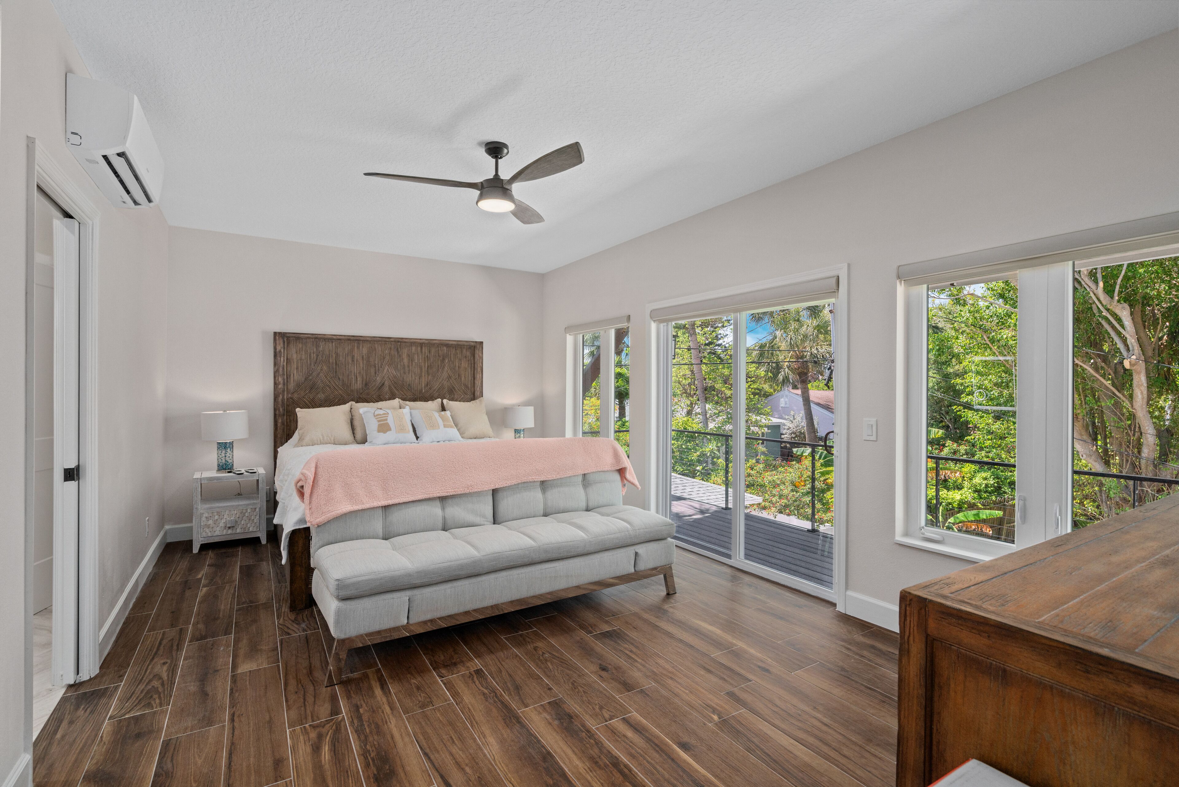 A bedroom with a large bed, a ceiling fan, and a view of the outdoors through large windows.