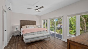 A bedroom with a large bed, a ceiling fan, and a view of the outdoors through large windows. - A Sunset Dream - Monthly Beach Rental (Clearwater Beach)