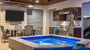 A modern outdoor kitchen with a built-in grill, a dining area with chairs, and a swimming pool with blue tiles. - A Sunset Dream - Monthly Beach Rental (Clearwater Beach)