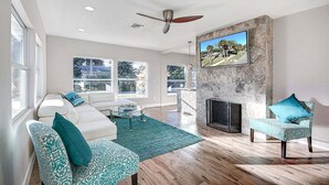 A spacious living room with a fireplace, large windows, and a ceiling fan. - A Sunset Dream - Monthly Beach Rental (Clearwater Beach)