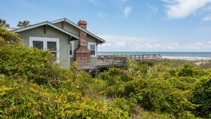 A beachfront house with a wooden deck and a view of the ocean.