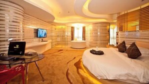Ein modernes Hotelzimmer mit gewölbter Decke, einer runden Sitzecke, einem großen Bett und einem Flachbildfernseher an der Wand.