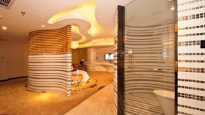Ein modernes Badezimmer mit gebogenem Design, einer Duschkabine aus Glas und einem an der Wand befestigten Fernseher.