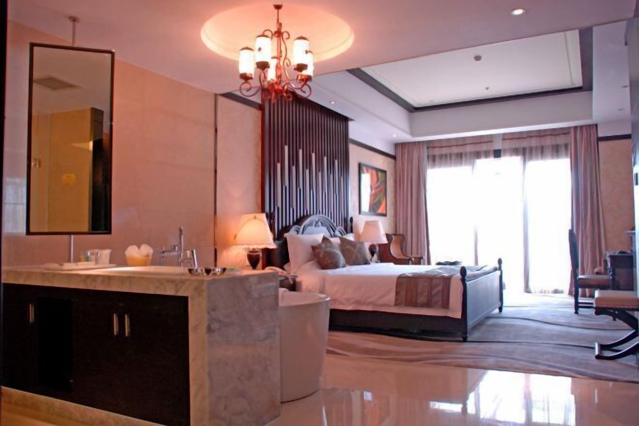 A modern hotel room with a large bed, a separate seating area, a vanity with a mirror, and a chandelier.