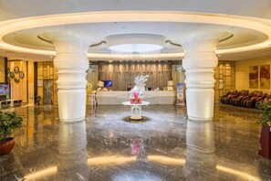 Un'ampia hall con una reception centrale, imponenti colonne bianche e un pavimento in marmo lucidato.