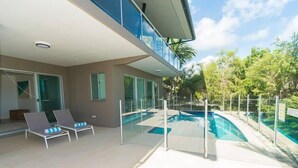 A modern house with a swimming pool, two lounge chairs, and a glass railing overlooking the pool.