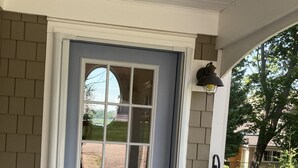 Una puerta azul claro con una ventana, un teclado de bloqueo y un pequeño porche con una silla negra y un tapete tejido azul.
