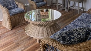 Un solárium con mobiliario de mimbre, una mesa de centro de vidrio y ventanas amplias.