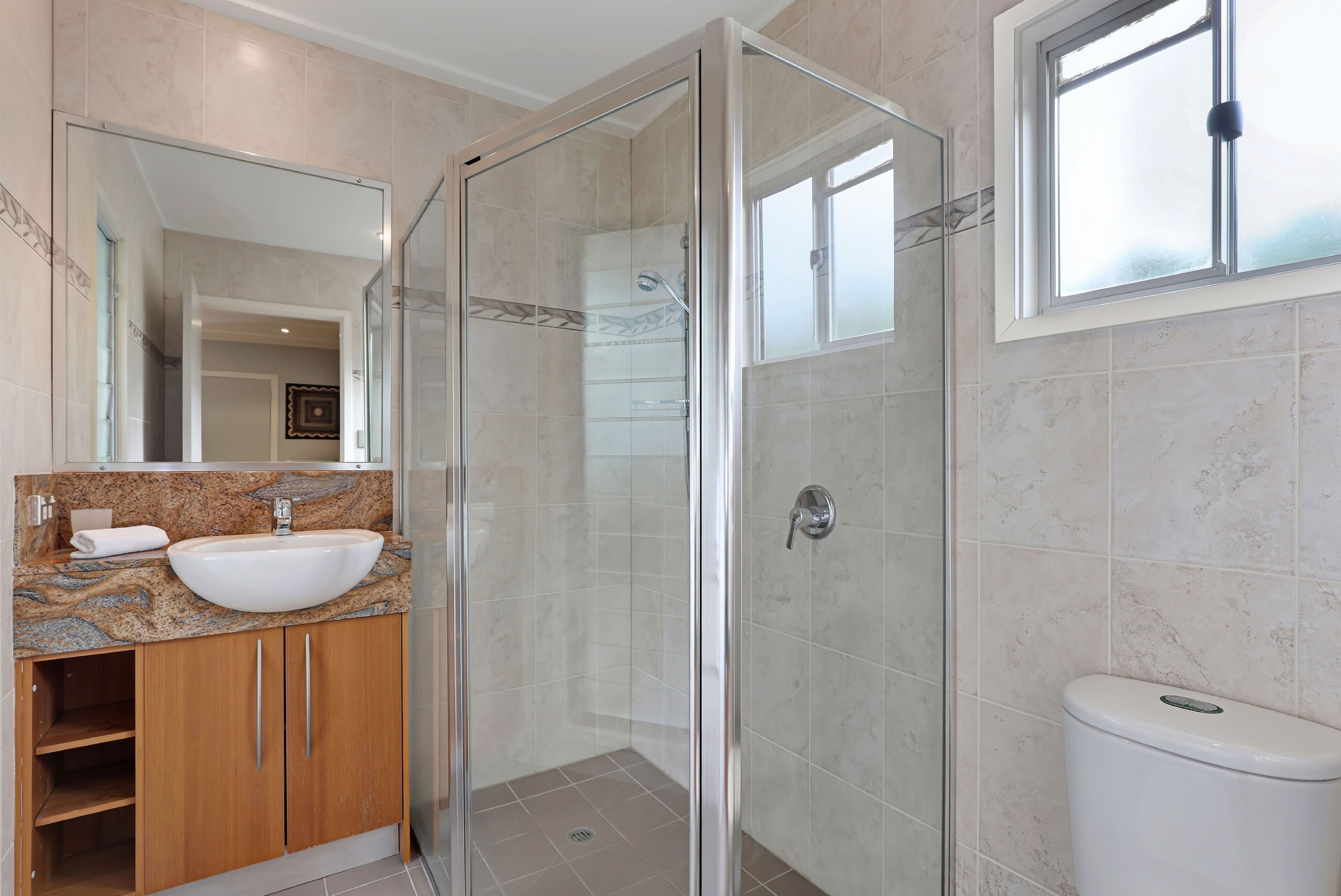 A bathroom with a glass-enclosed shower, a sink with a marble countertop, and a toilet.